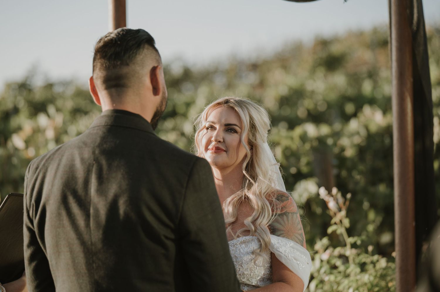 Intimate wedding moment captured between newlyweds in a sunlit vineyard setting.