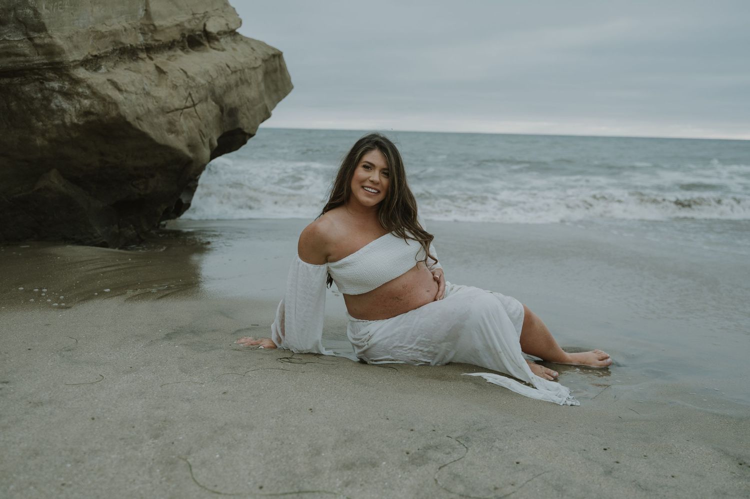 Seaside maternity photography with dramatic coastal rock formations.