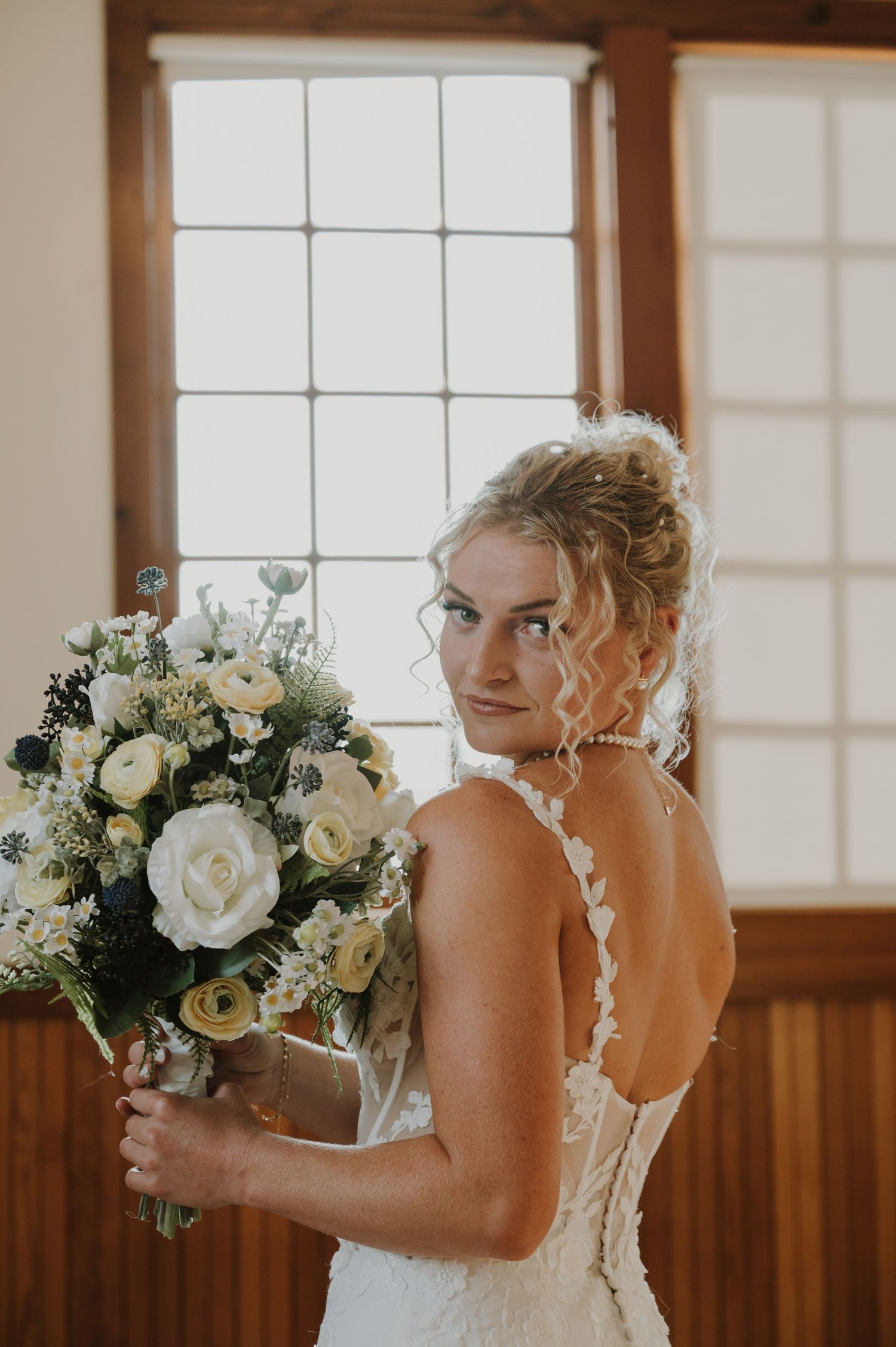 Beautiful white rose wedding bouquet held against a wooden paneled wall in natural light.