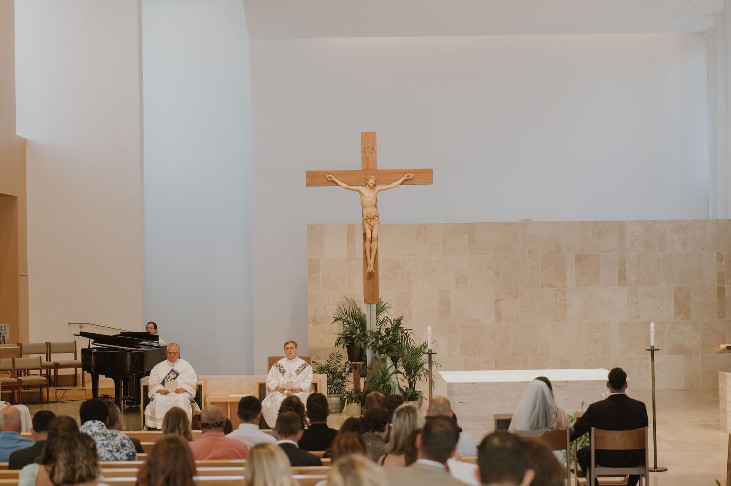 Wedding ceremony at a modern Catholic church with a crucifix and guests seated in pews.