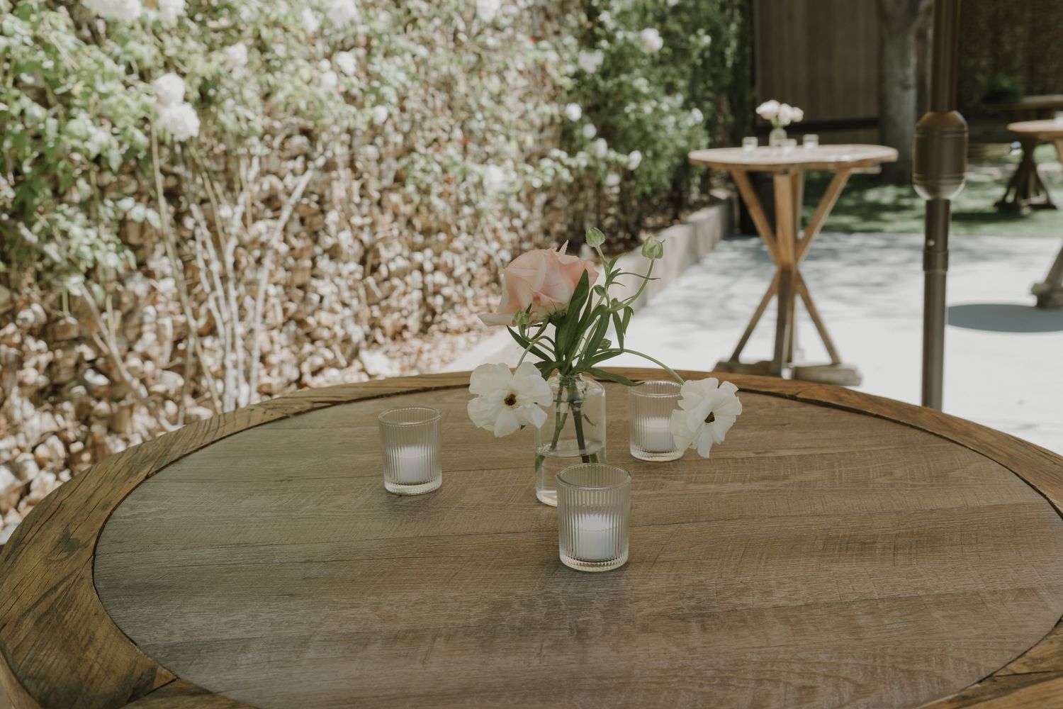 Rustic wooden barrel table with white flowers and candles at an outdoor wedding reception.