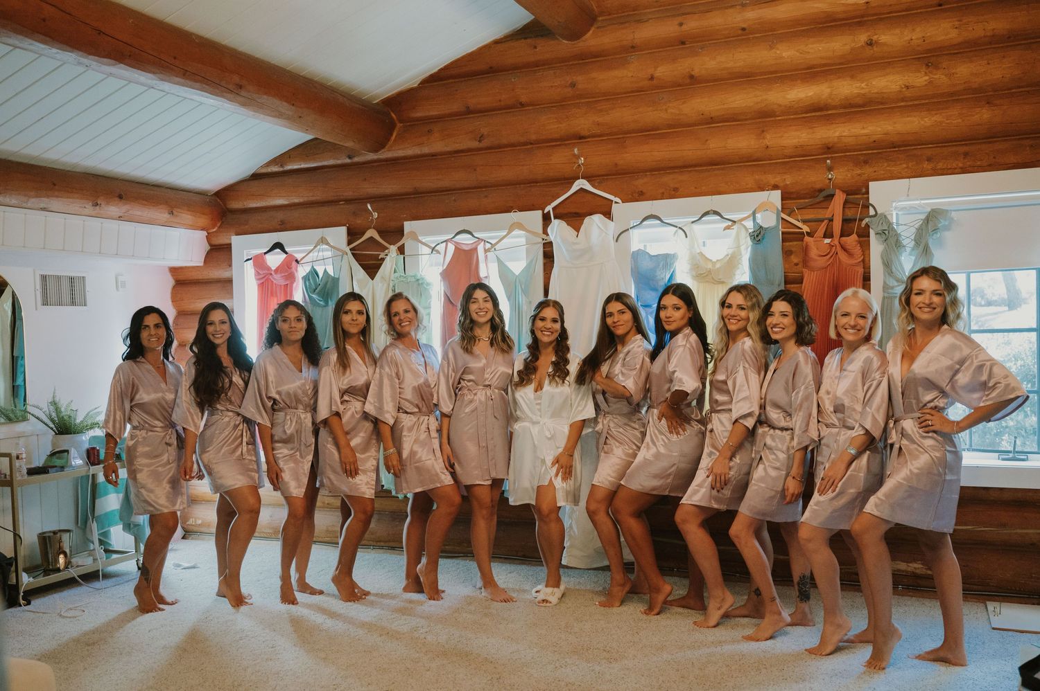 Group of bridesmaids in matching satin robes posing together in a rustic wood-beamed room.