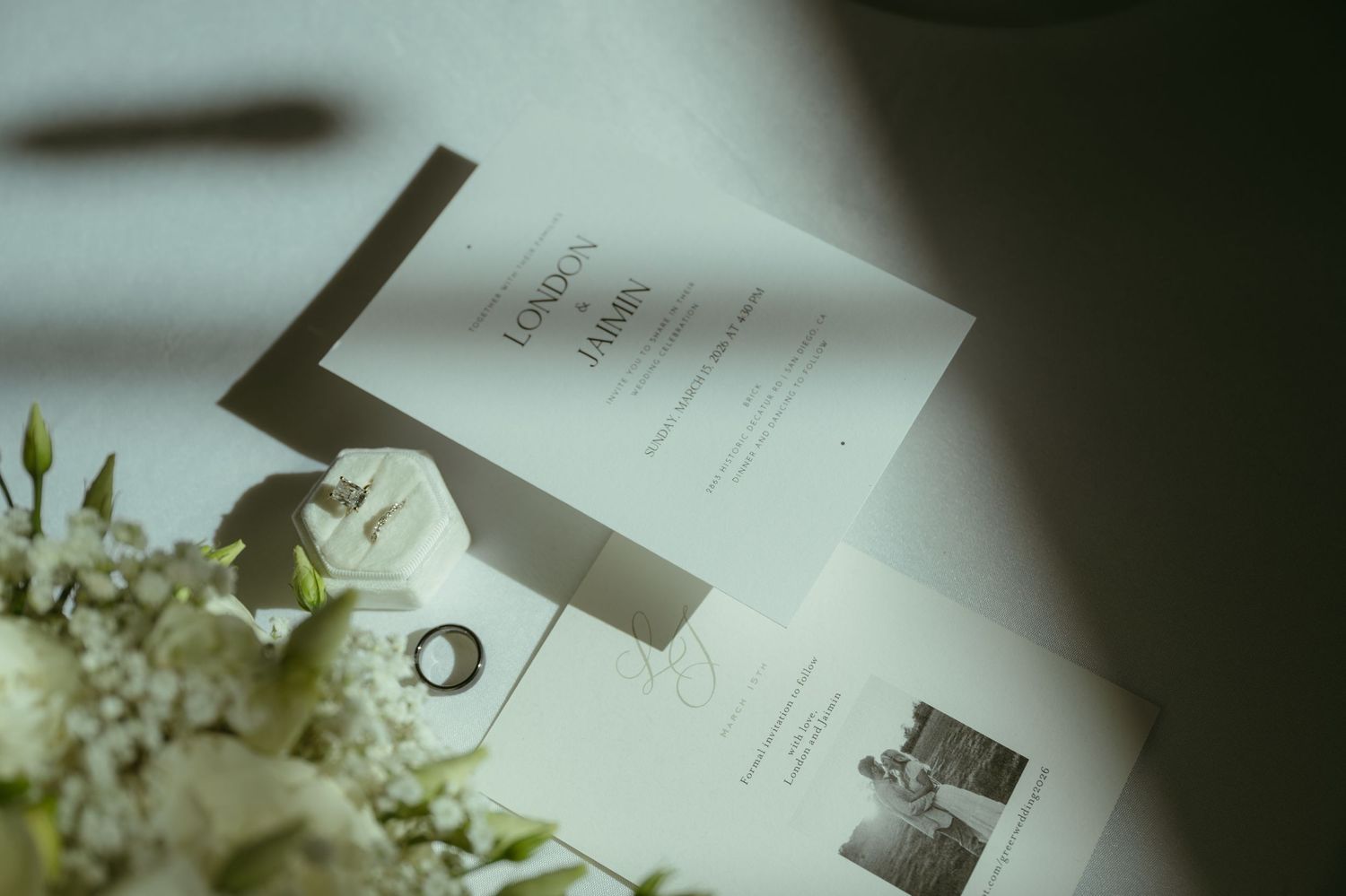 Elegant wedding stationery with rings and white floral bouquet on a light surface.