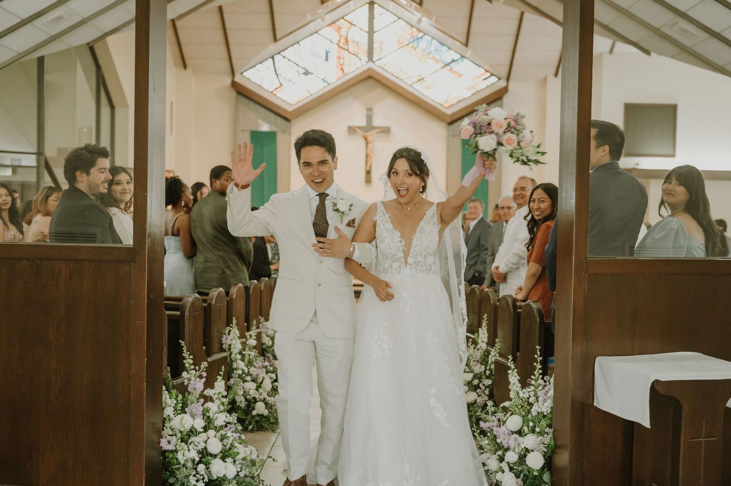 Newlyweds celebrate walking back down the aisle in a sunlit chapel after their wedding.