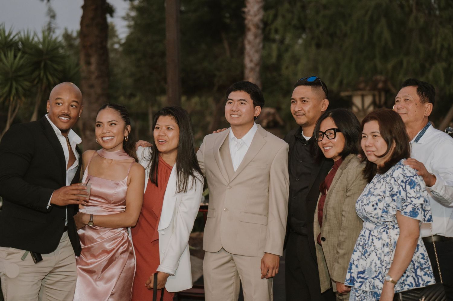 Group of elegantly dressed wedding guests posing together outdoors at a garden wedding celebration.