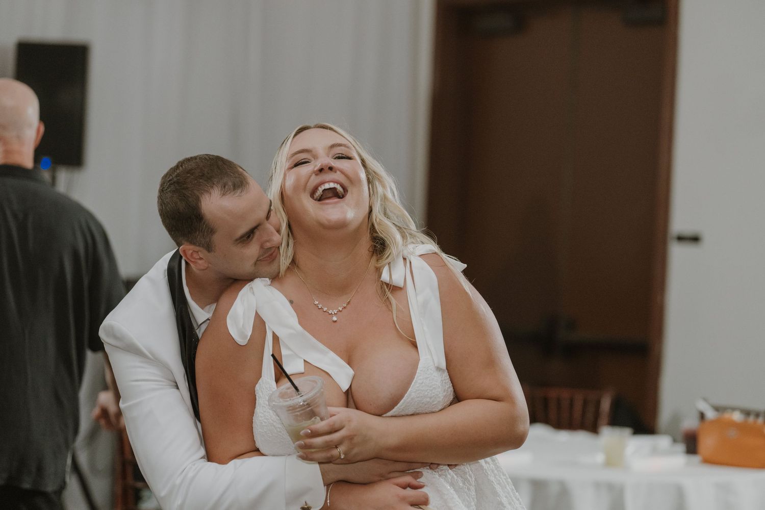 Groom kisses laughing bride on the cheek during their joyful wedding reception celebration.