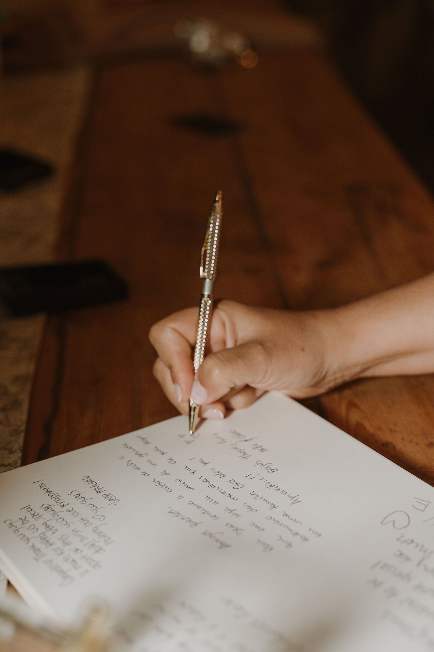 A hand writing notes in a journal with a gold pen on a wooden table.