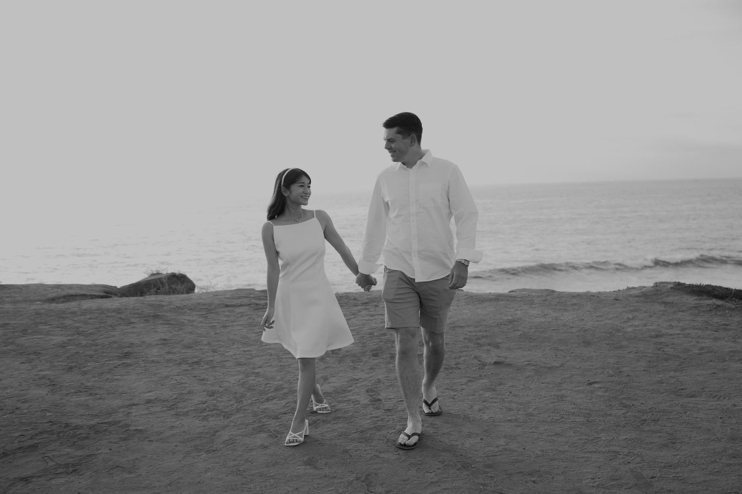 Couple walking along a coastal cliff at sunset in white attire.