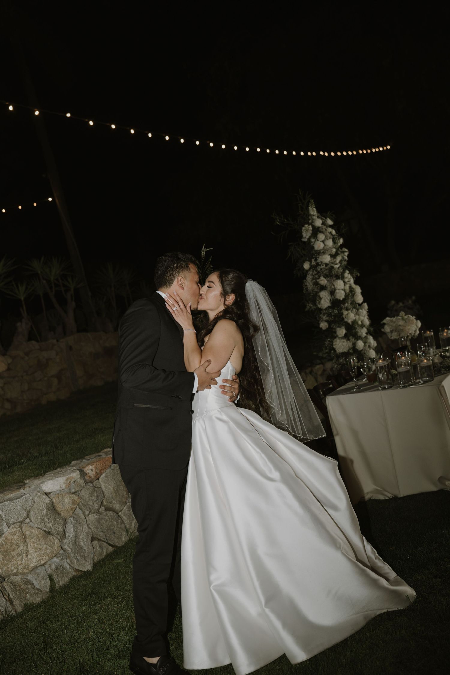 Romantic nighttime wedding scene with string lights and elegant white decor.