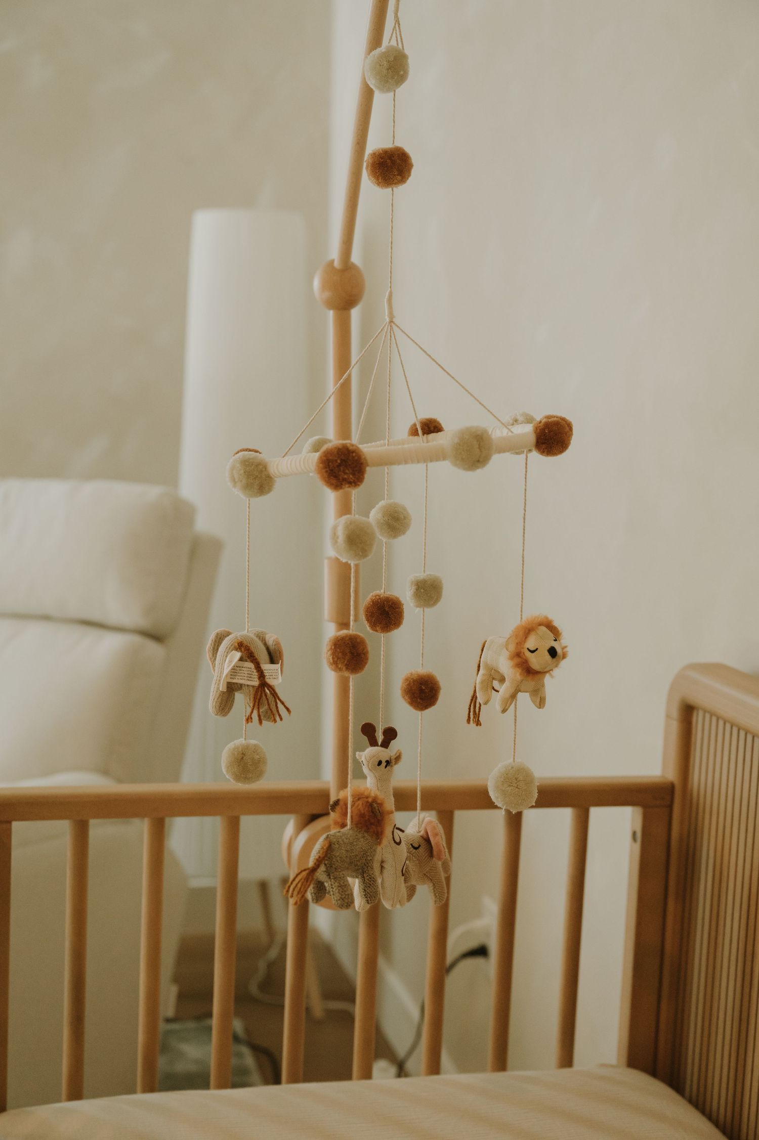 Wooden crib with neutral toned mobile hanging above.