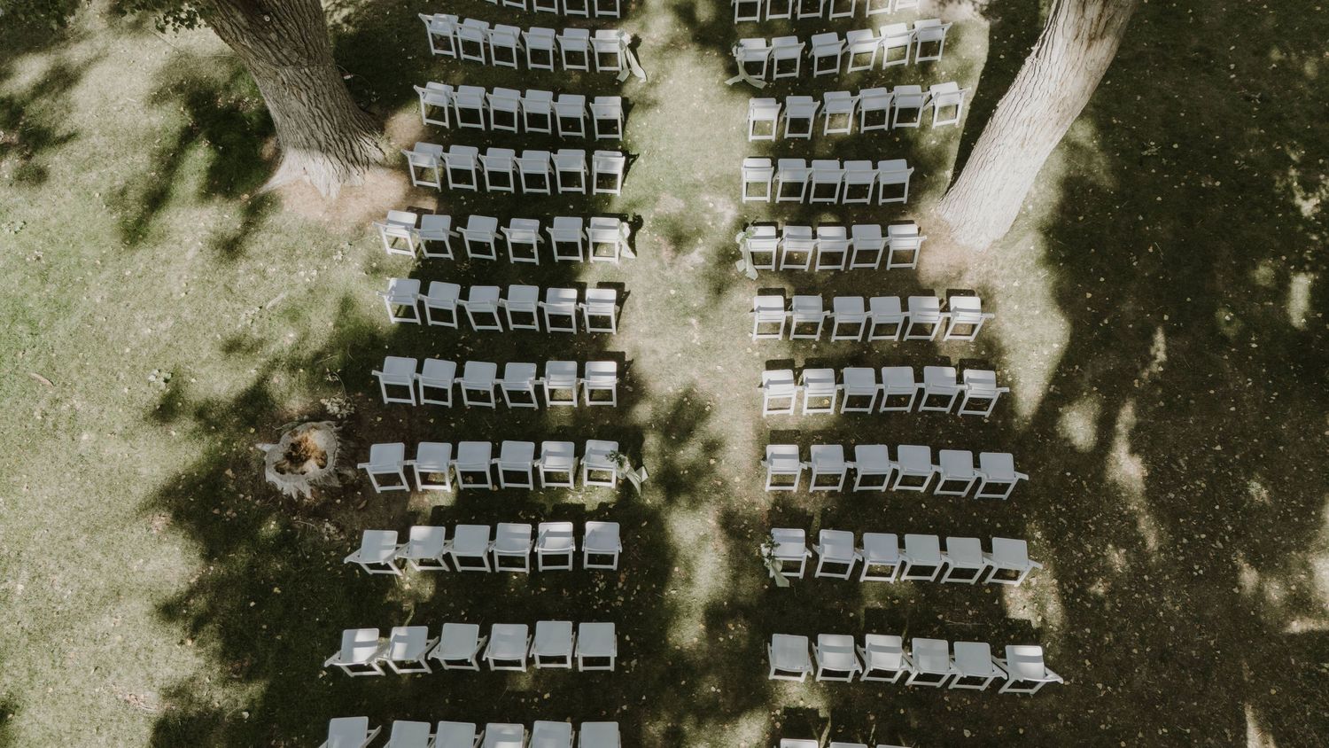 Aerial view of white wedding ceremony chairs arranged symmetrically on a lawn.