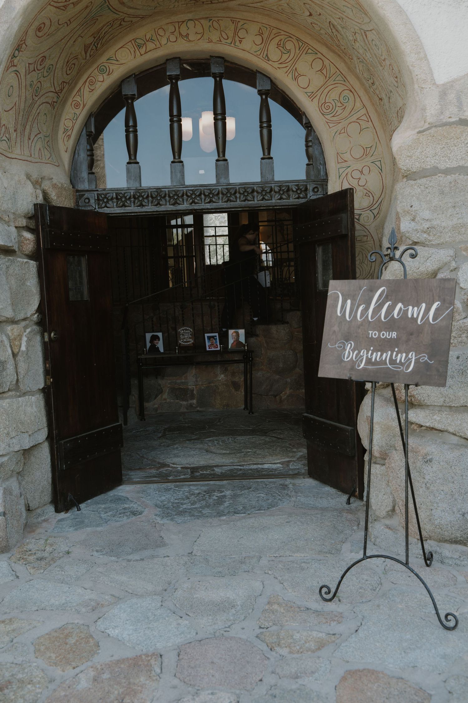 Elegant wedding venue entrance with ornate stone arch, open wooden doors, and a decorative Welcome to Our Beginning sign.