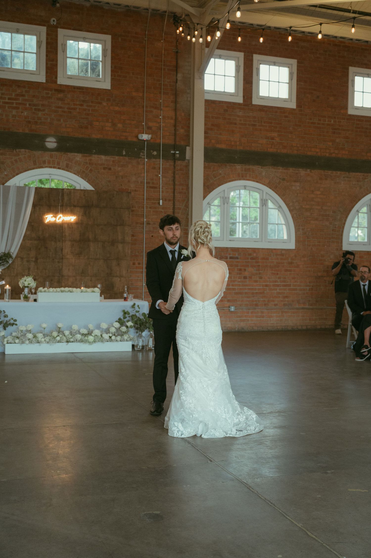 Bride and groom share their first dance in a rustic brick venue with string lights at their wedding reception.