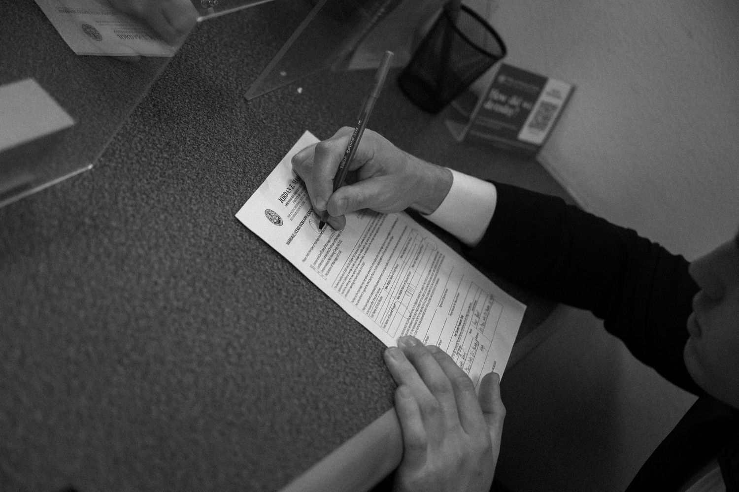 Black and white images showing hands signing documents at a wedding ceremony.