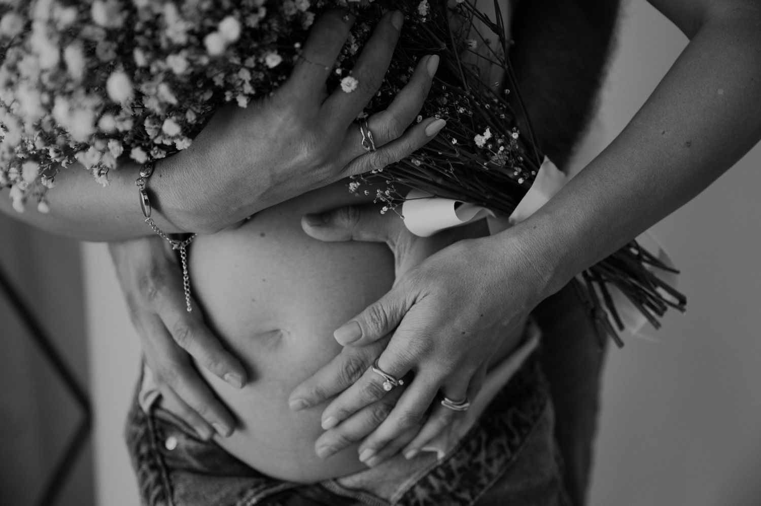 Black and white photo of hands cradling a pregnant belly with flowers.