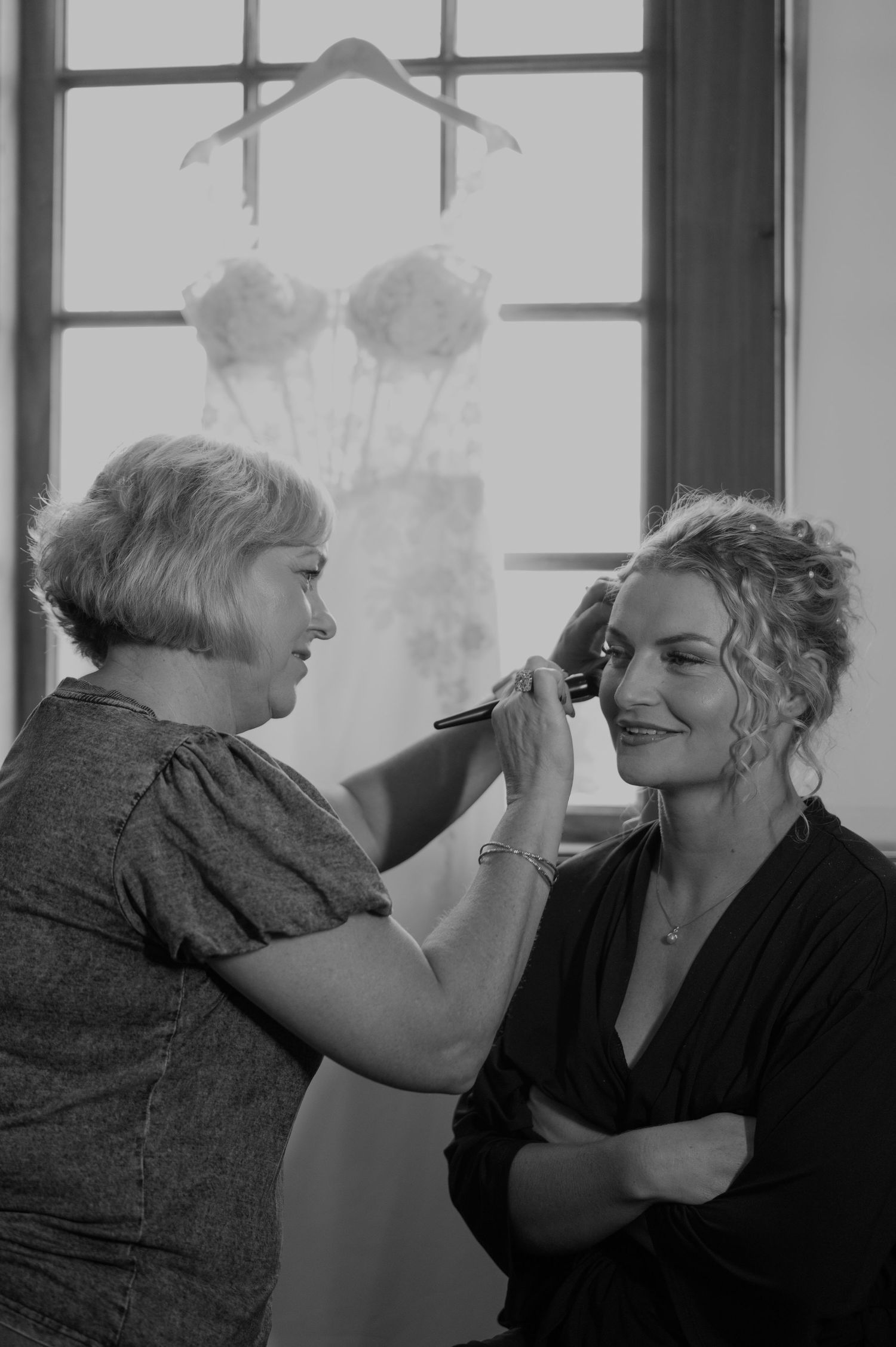 Black and white image of wedding day makeup preparation in front of a window.