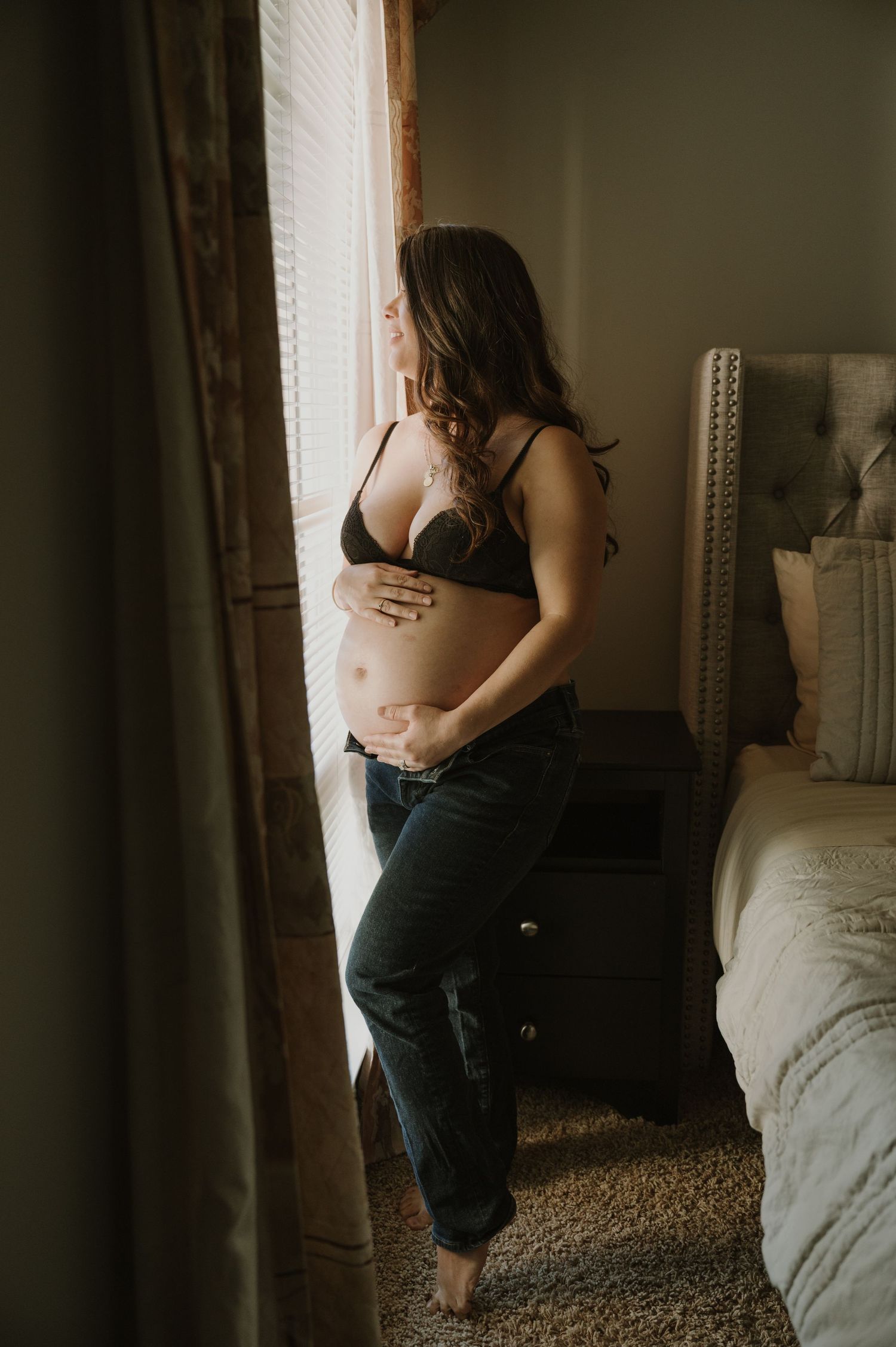 Artistic boudoir photoshoot in a sunlit bedroom with natural window light.