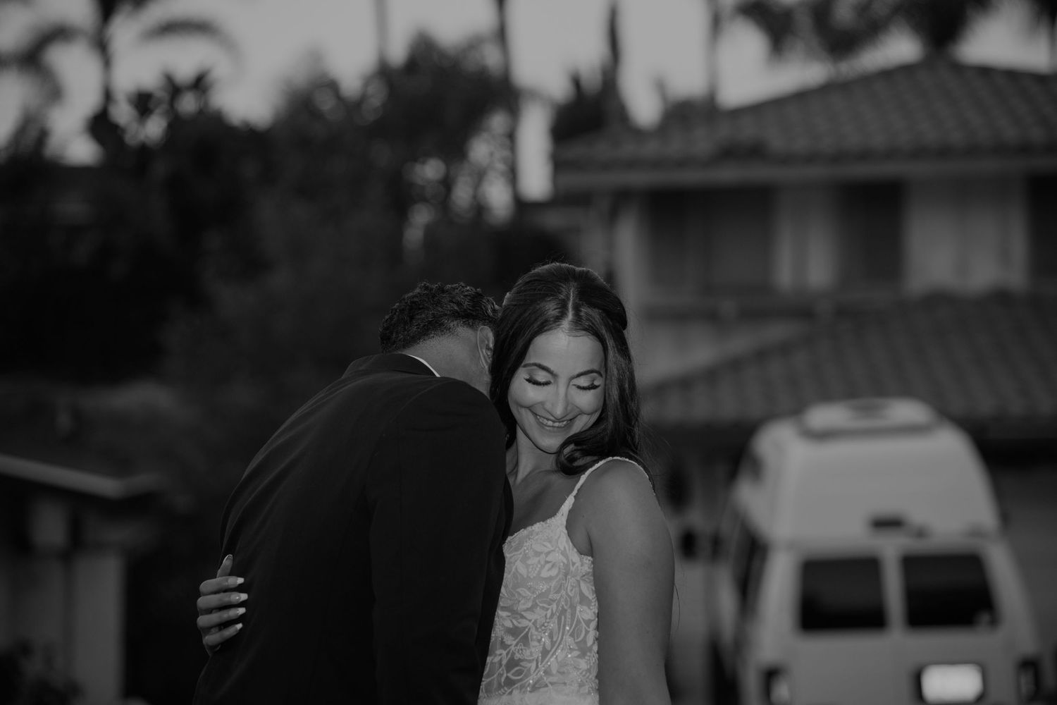Black and white photo of a couple sharing a tender moment outdoors, bride smiling as groom kisses her cheek.