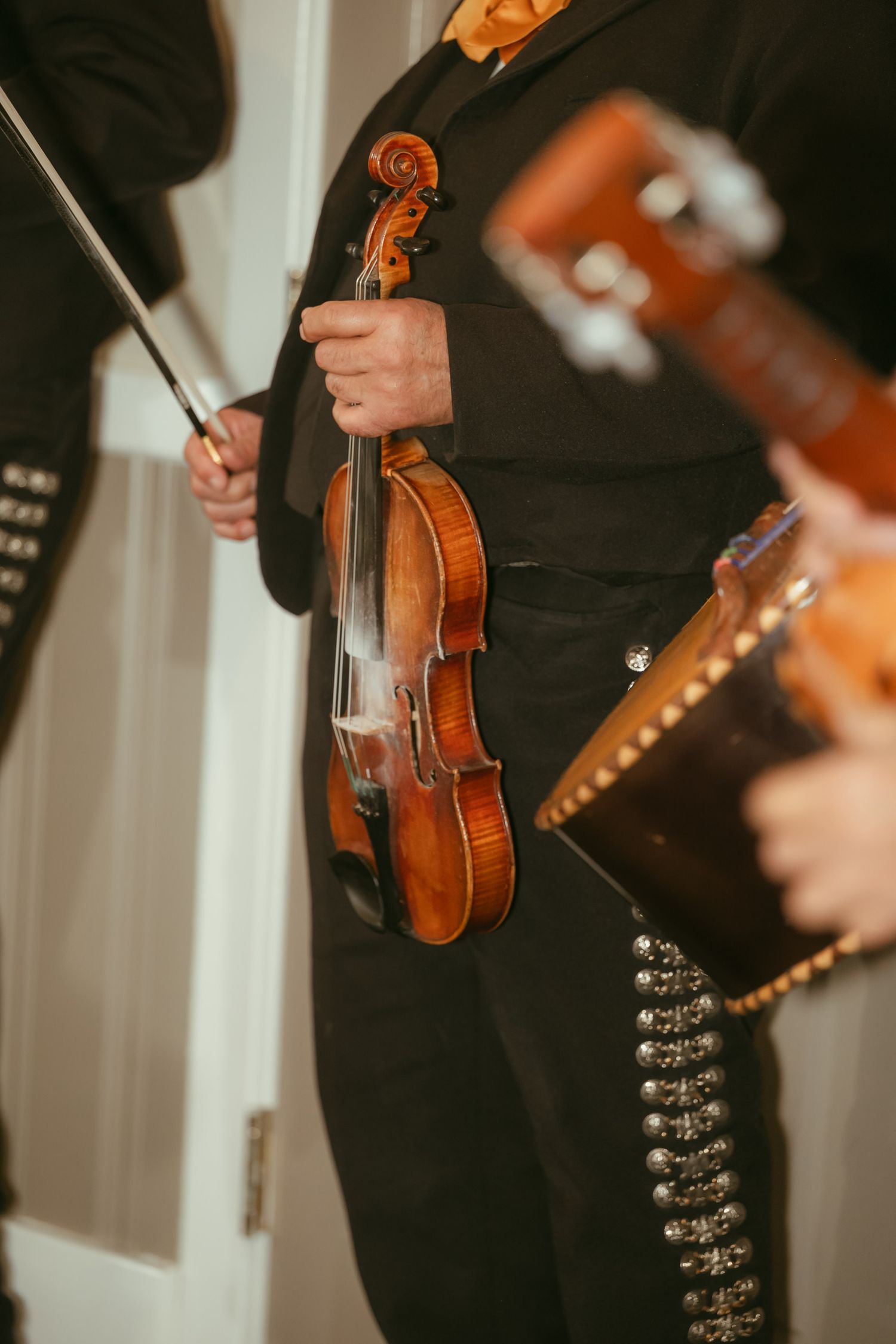 Mariachi musician in black suit holding a violin and bow at a wedding celebration.