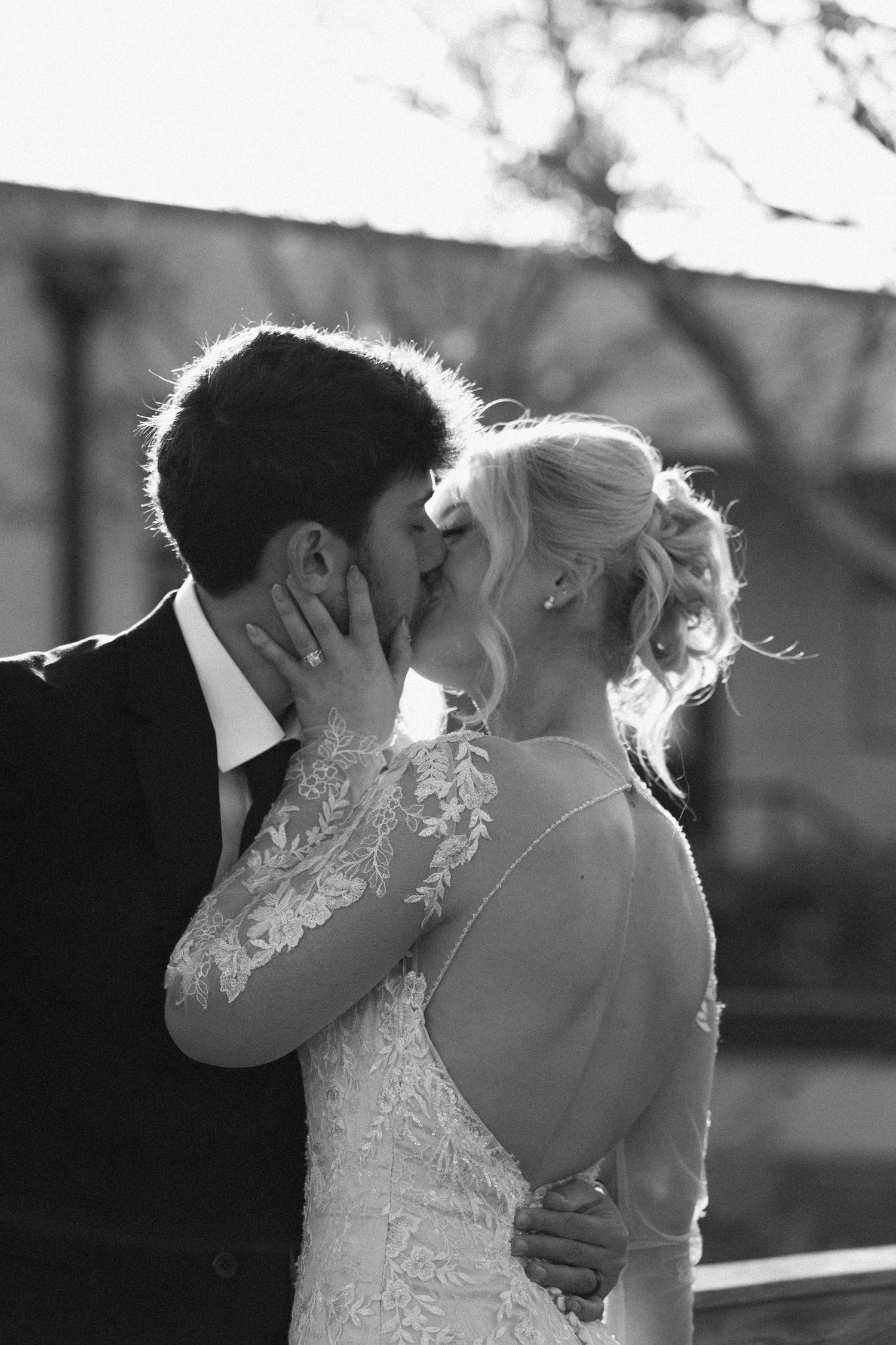 Black and white photo of a bride and groom sharing a romantic kiss outdoors on their wedding day.