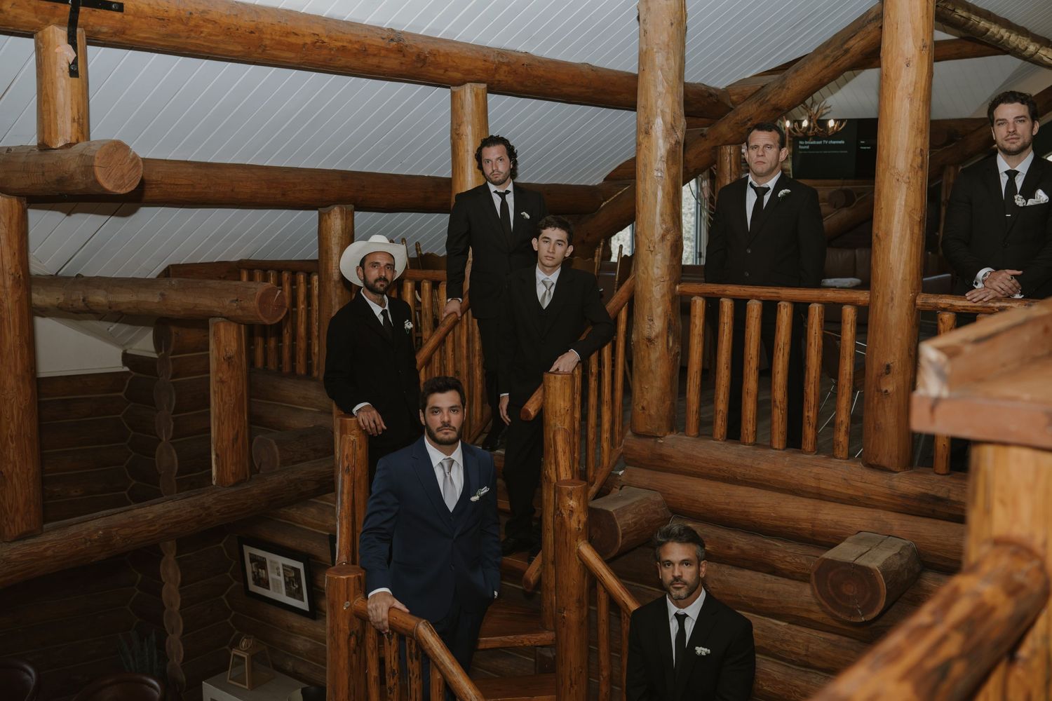 Groom and groomsmen posed on a rustic log staircase inside a wooden cabin wedding venue.