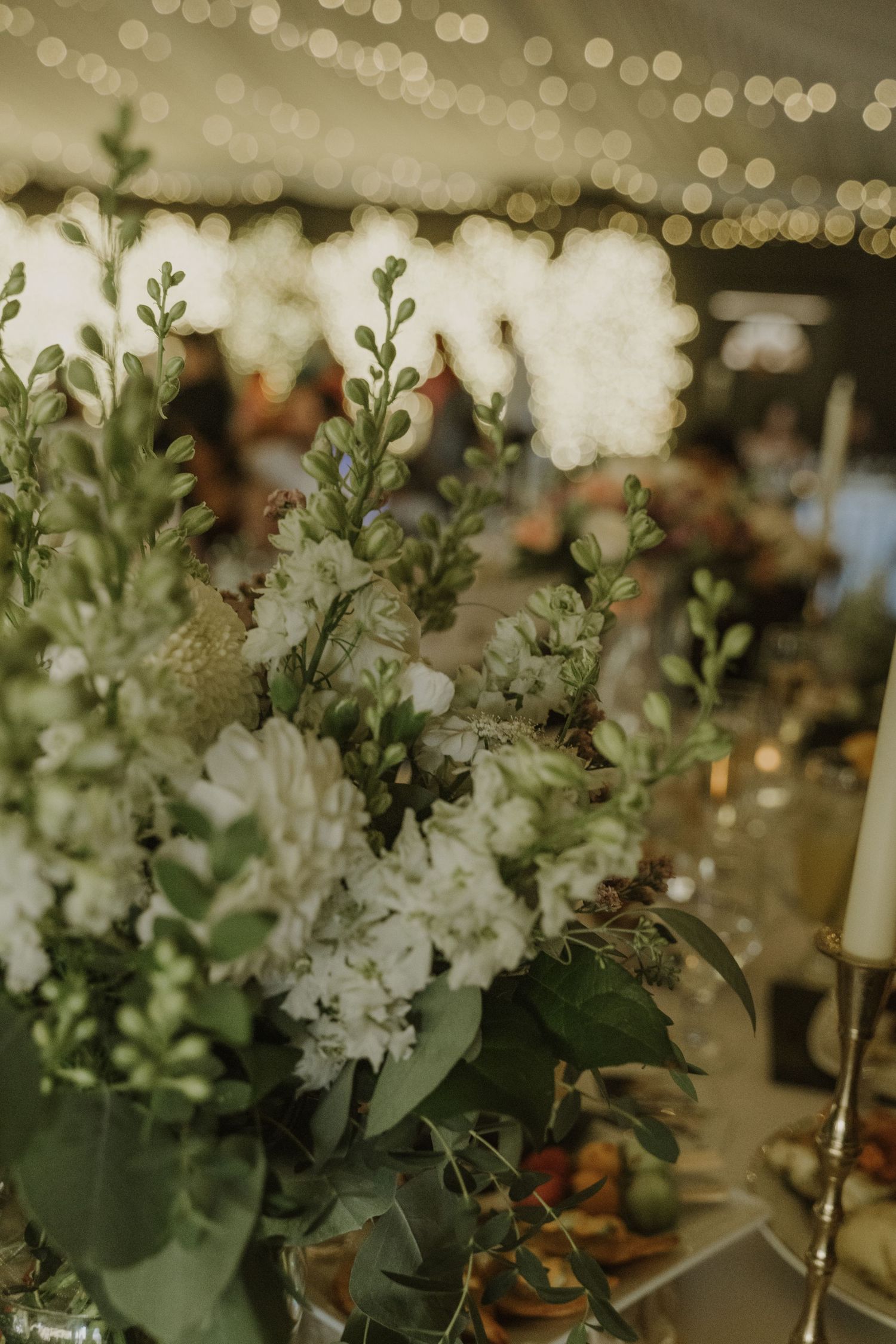 Elegant white floral centerpiece with greenery and hydrangeas glowing under warm bokeh fairy lights.