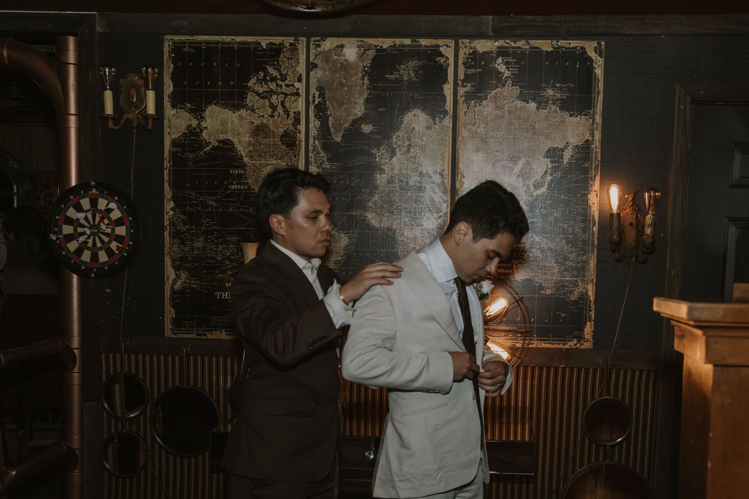 Two men in suits share a tender moment in a dimly lit vintage room with rustic decor.