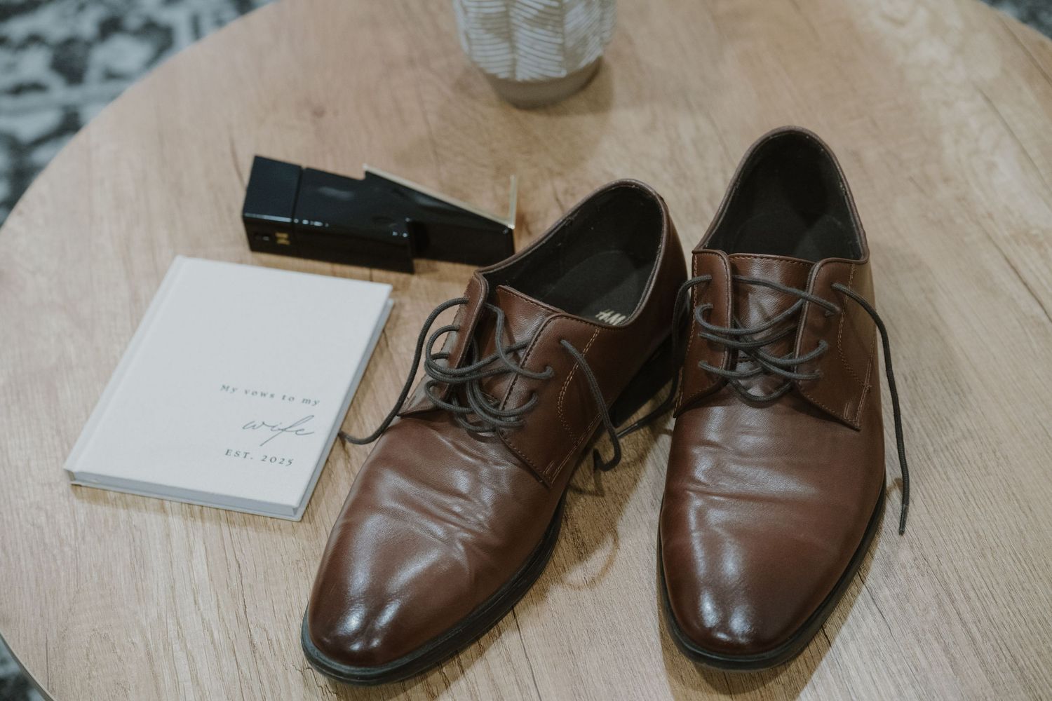 Brown leather lace-up dress shoes on wooden table with cologne and small notecard, perfect for formal occasions.