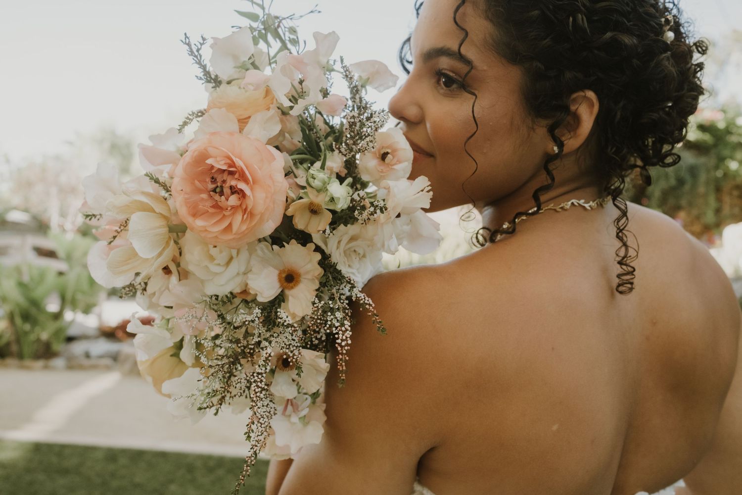 Bride in a strapless wedding gown holding a beautiful blush and white floral bouquet over her shoulder.