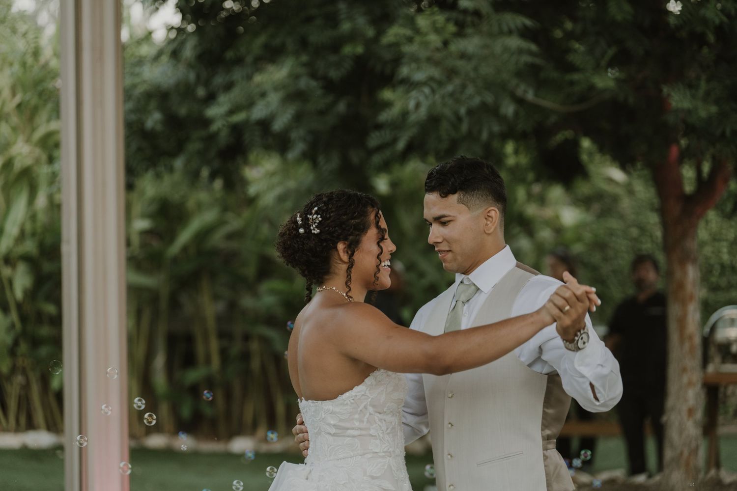 Bride and groom share their first dance outdoors surrounded by lush greenery at their wedding reception.