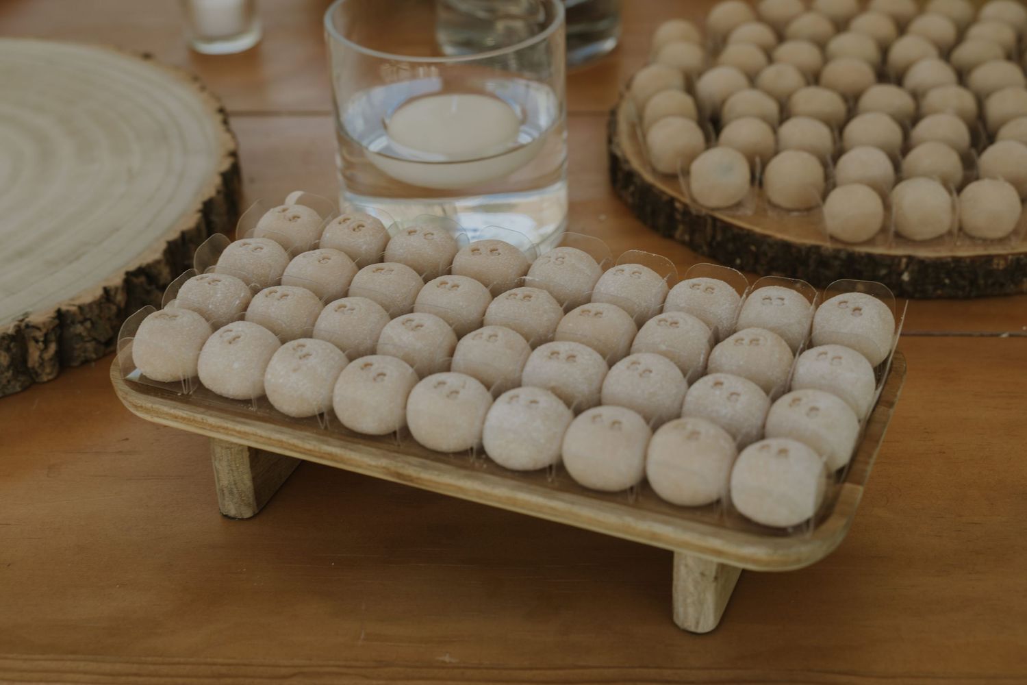 Small round white cake pops displayed on a wooden tray with legs at a wedding reception.