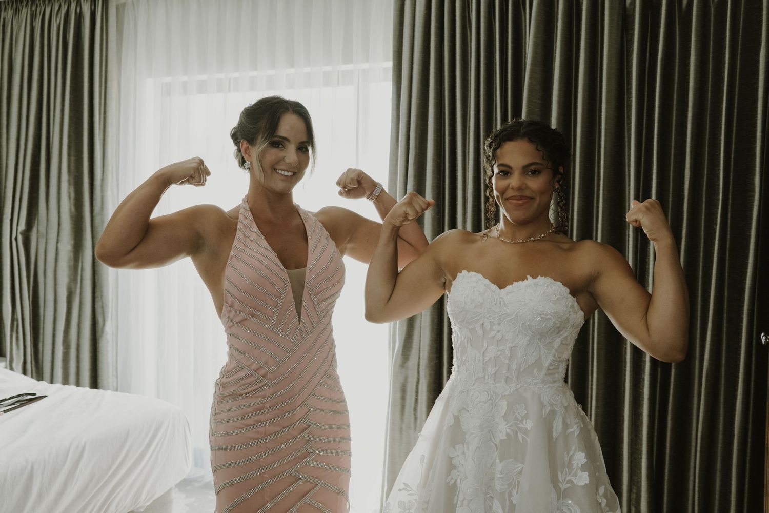 Bride and bridesmaid flexing muscles together in a hotel room before the wedding.