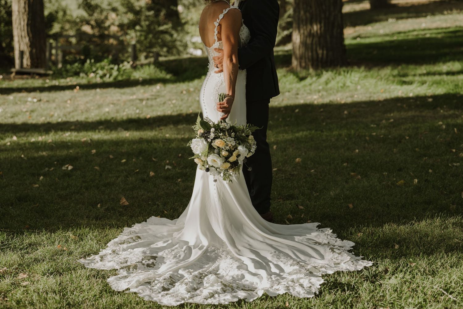 A beautiful wedding dress train trails across green grass during an outdoor ceremony.