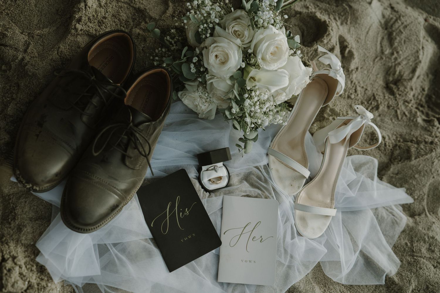 Wedding details including white roses and delicate accessories arranged on textured surface.