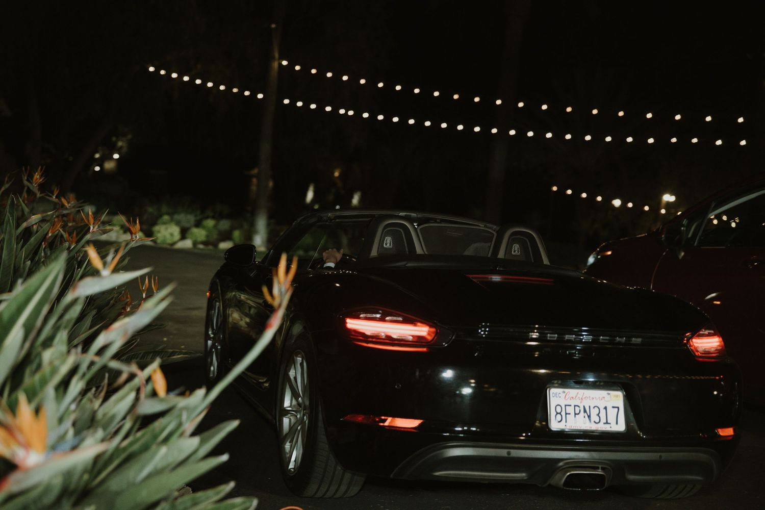 Black car parked at night under string lights creating a romantic ambiance.
