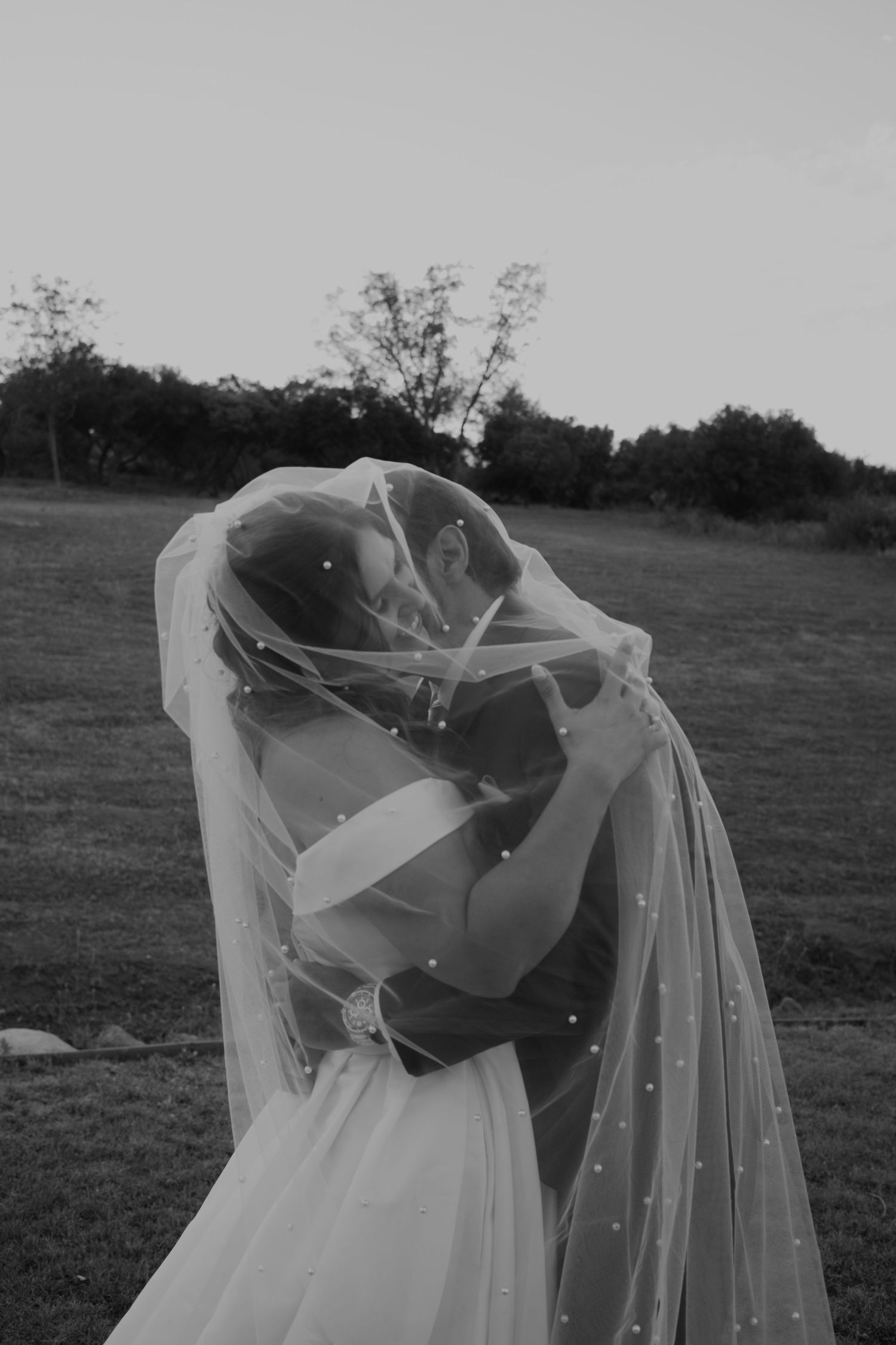 Flowing white wedding veil with pearl details billowing in the breeze against a grey background.