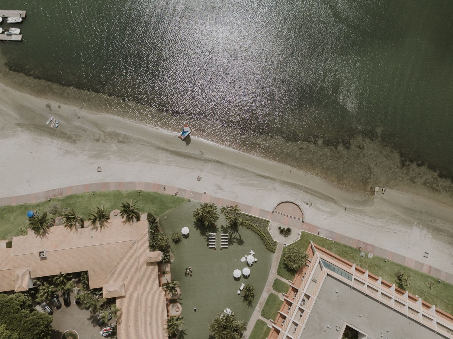 Aerial view of a waterfront wedding venue with palm trees and white chairs.