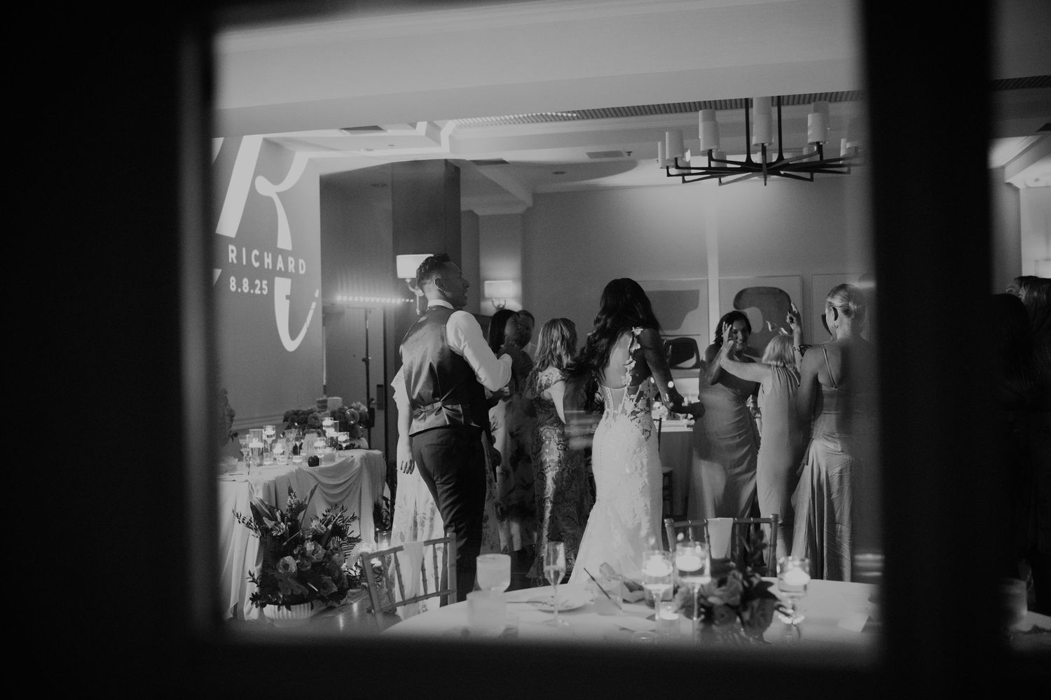 Black and white photo of a wedding reception venue with elegant lighting and decor.