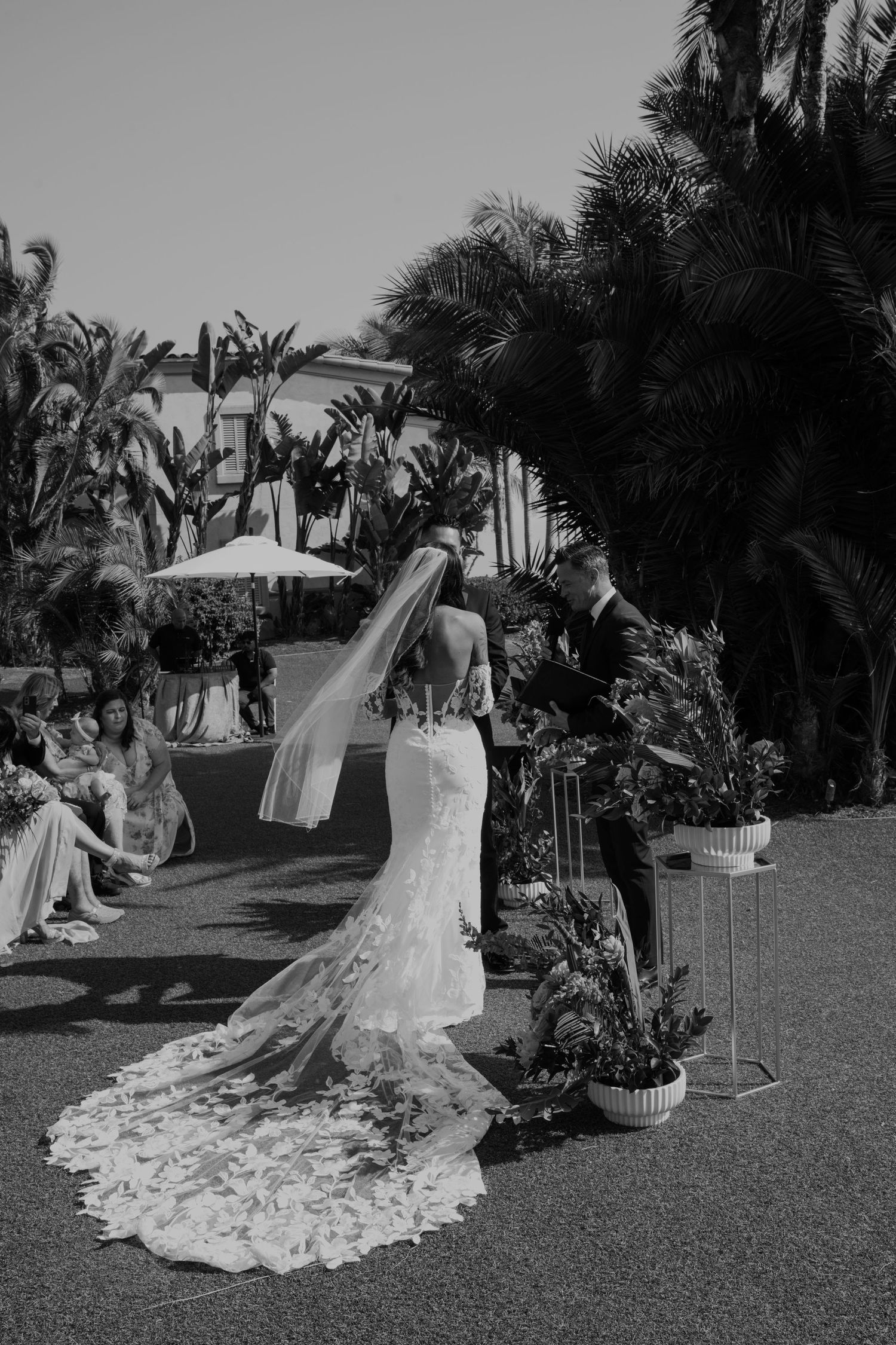 Black and white photos of a bride in a lace wedding dress with long train in a tropical garden setting.