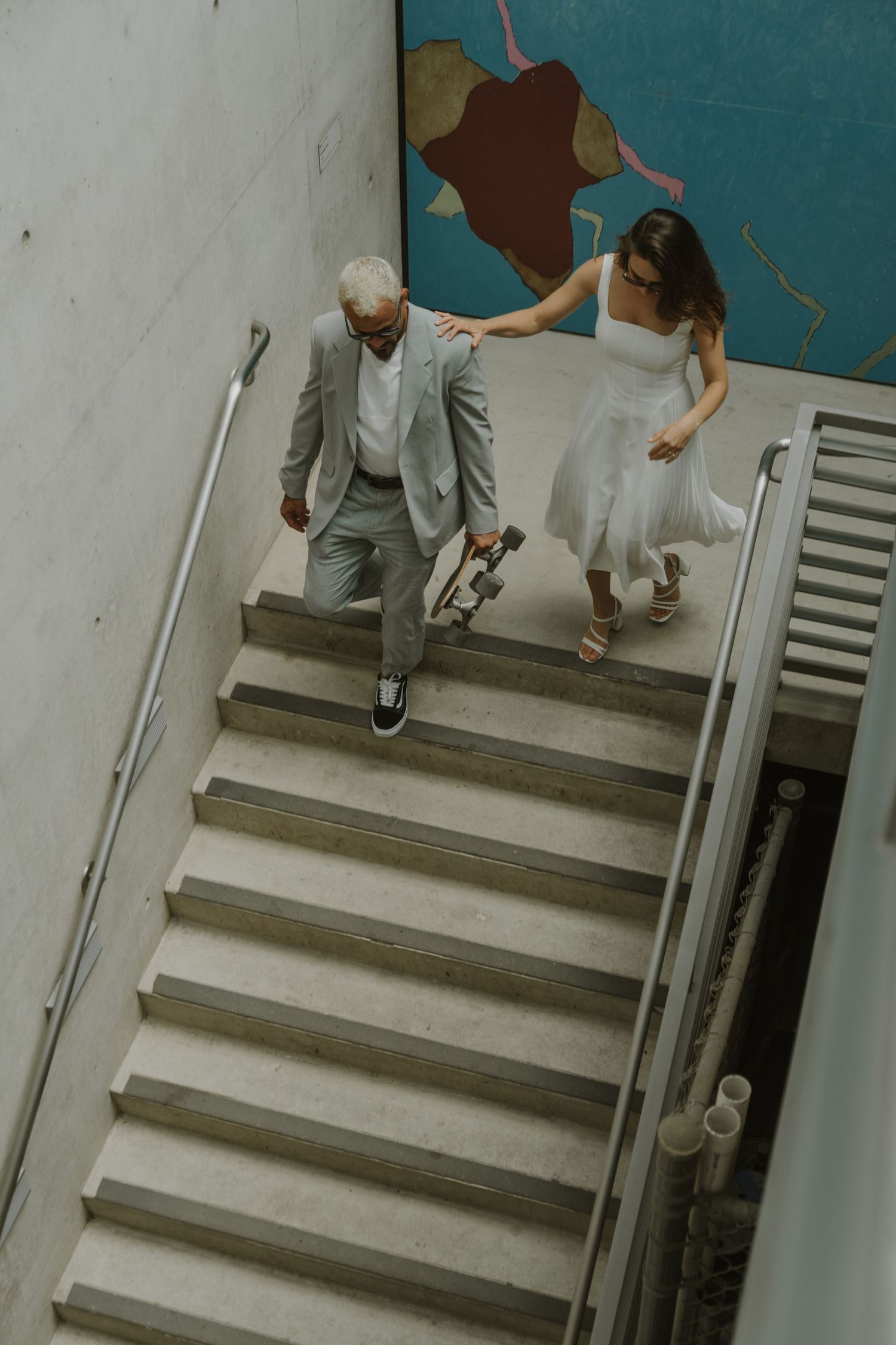 Two people walking down concrete steps together in formal attire.