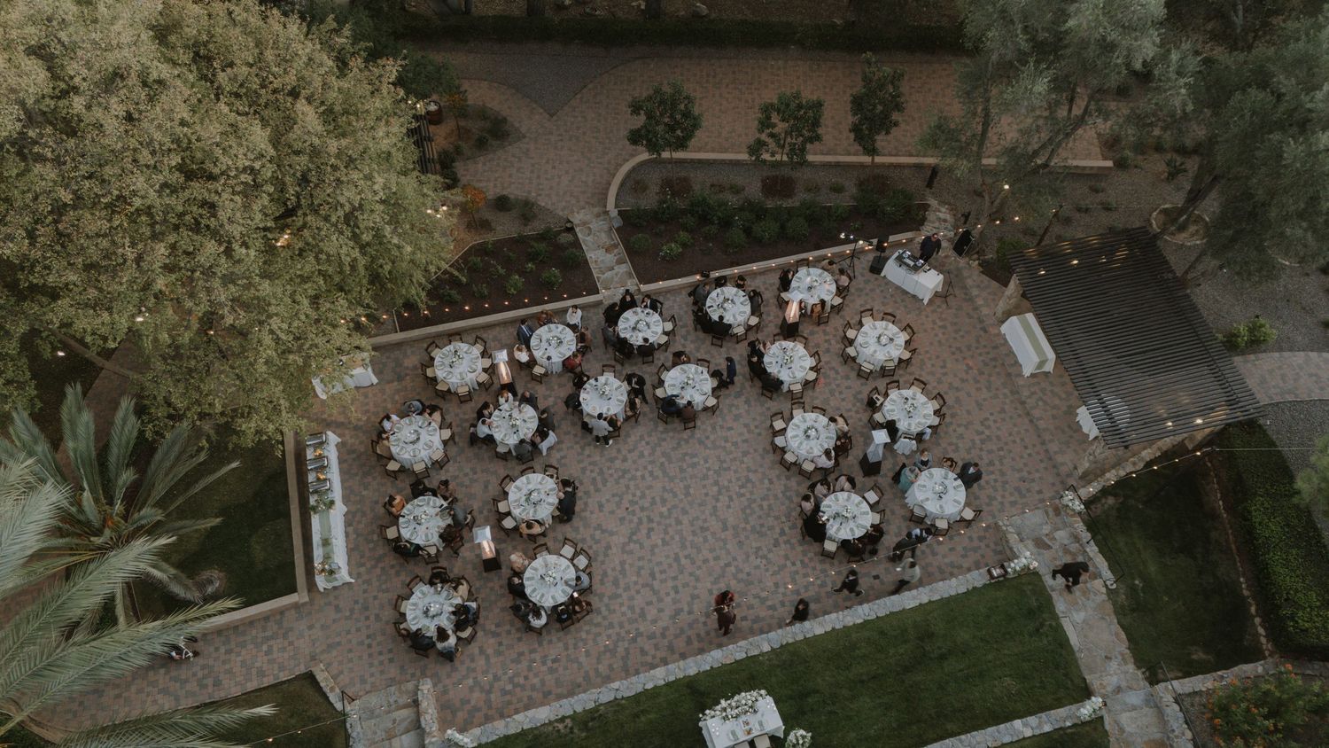 Aerial view of an outdoor wedding venue with round tables arranged on a stone patio.