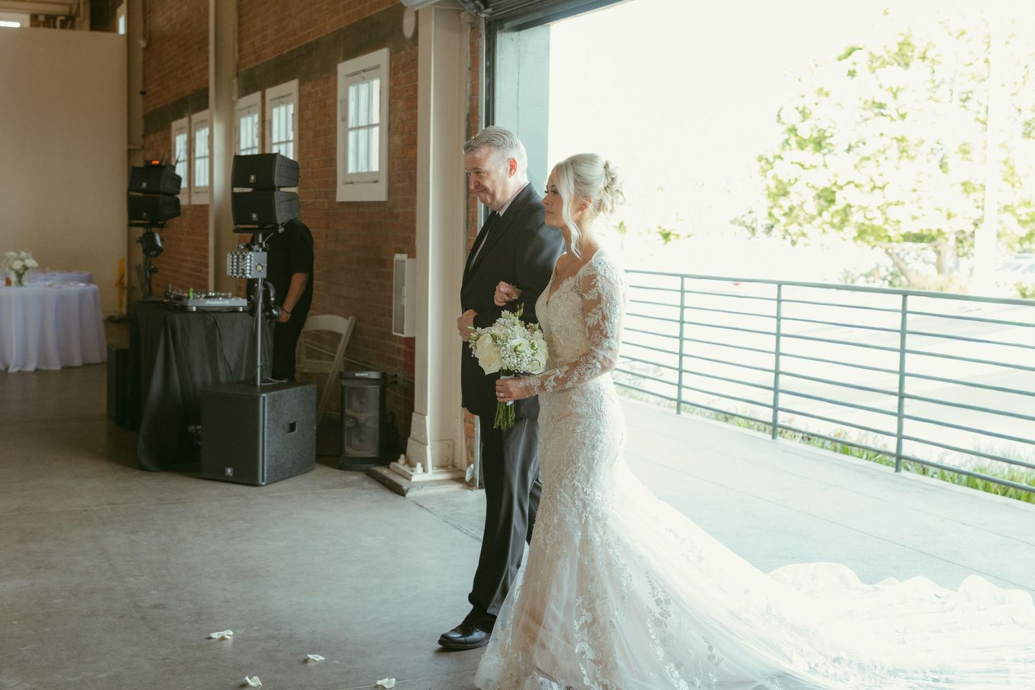 Bride in elegant lace gown shares quiet moment with escort before wedding ceremony.