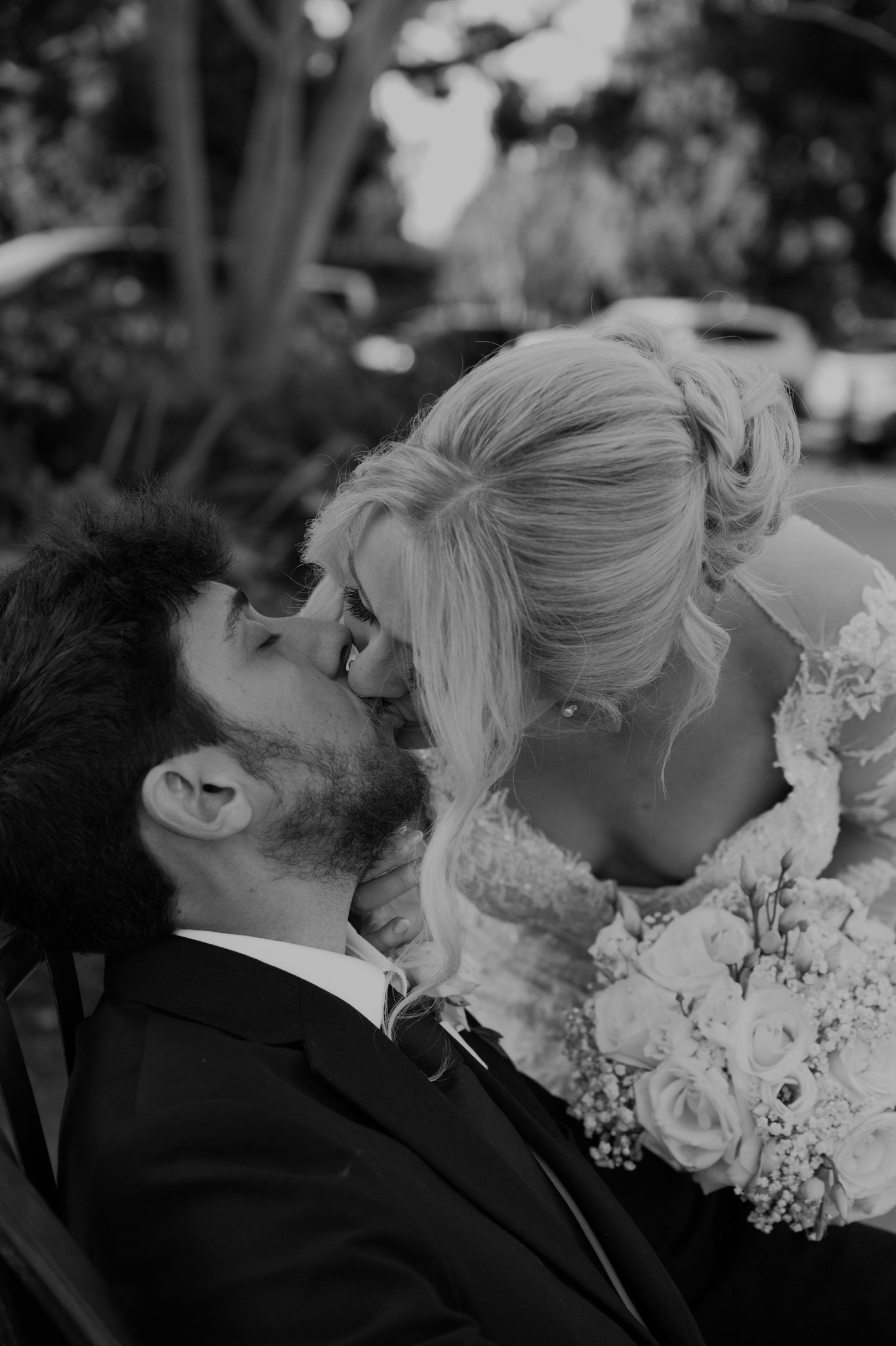 Black and white photo of bride and groom sharing a romantic kiss, bride holding white rose bouquet.