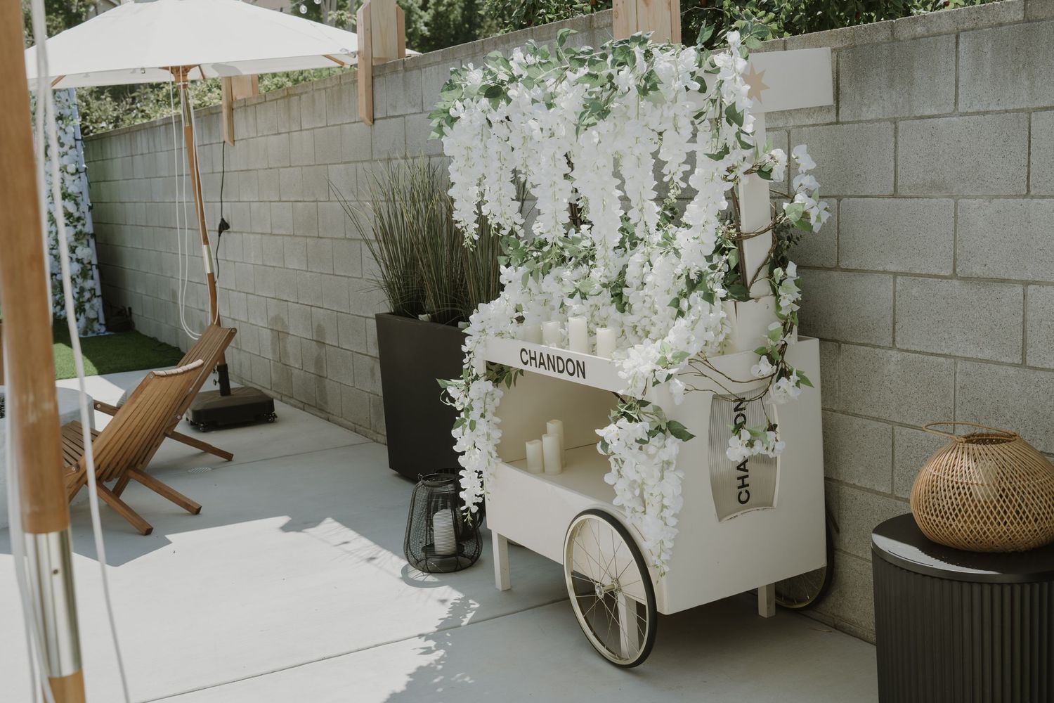 Elegant white Chandon champagne cart adorned with cascading white floral arrangements on a patio.