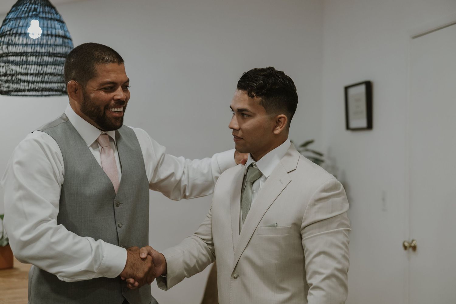 Two men in wedding attire sharing a warm handshake and smile before the ceremony.
