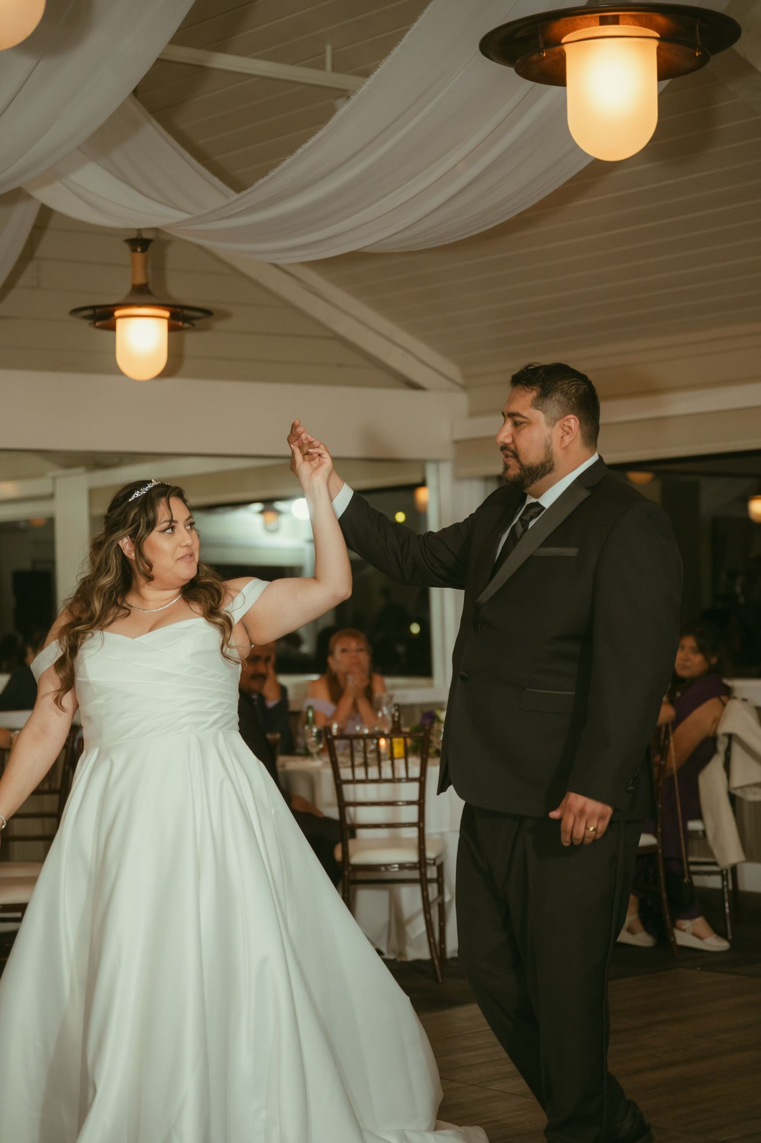 Bride and groom share their first dance under warm pendant lights at wedding reception venue.