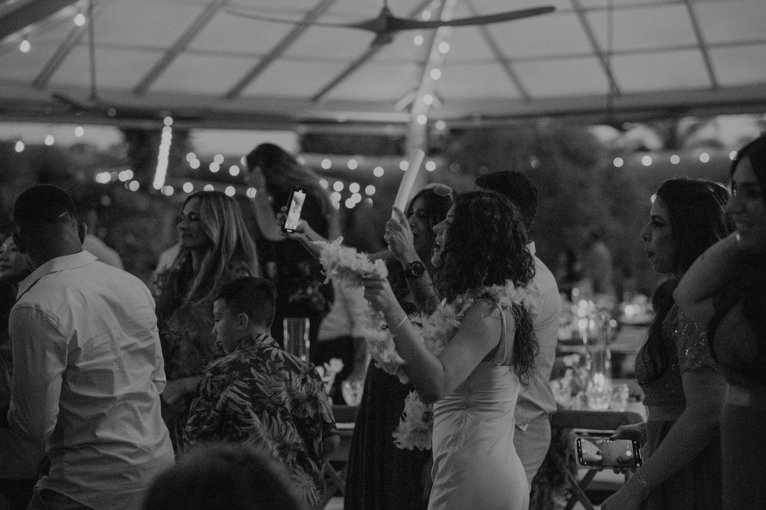 Wedding guests dance and celebrate together under string lights at an evening reception.