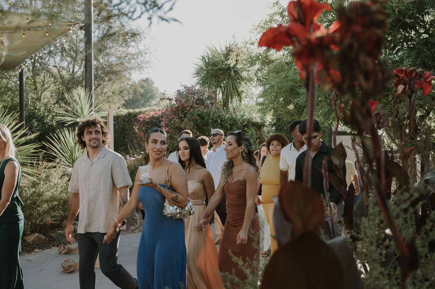 Wedding guests and bridesmaids in colorful dresses walking through outdoor ceremony venue.
