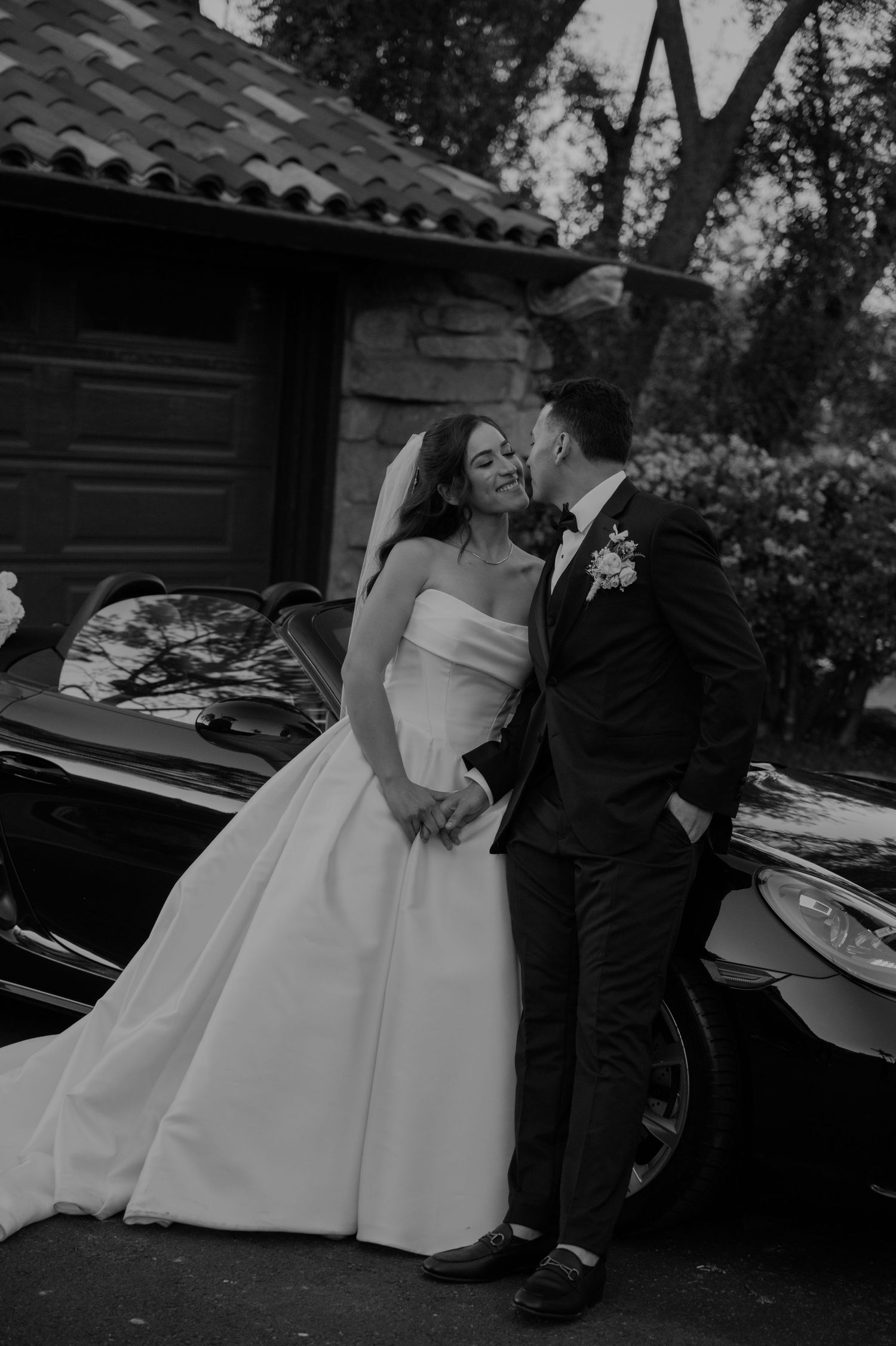 A series of black and white wedding photos showing romantic moments near vintage cars.