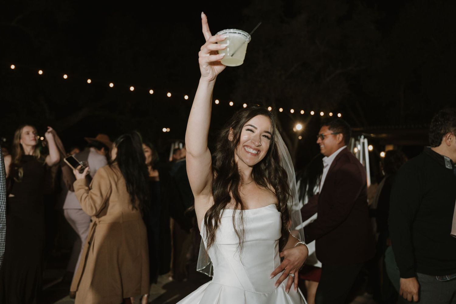 Wedding celebration under string lights with guests dancing.